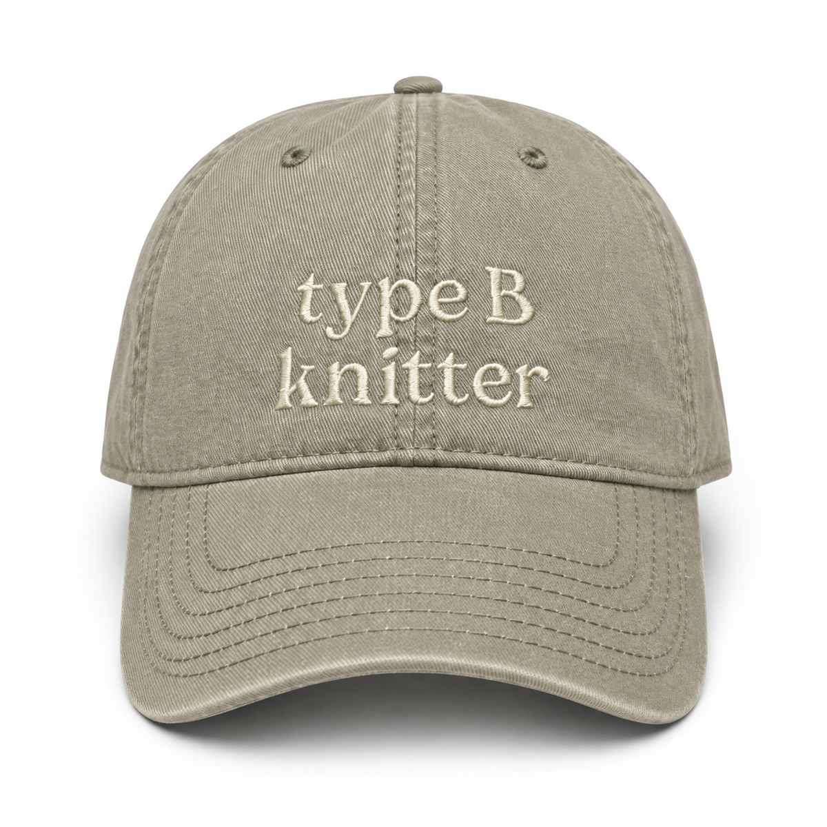 A light khaki cotton baseball cap with 'type B knitter' embroidered in cream-colored text on the front, shown against a plain white background.