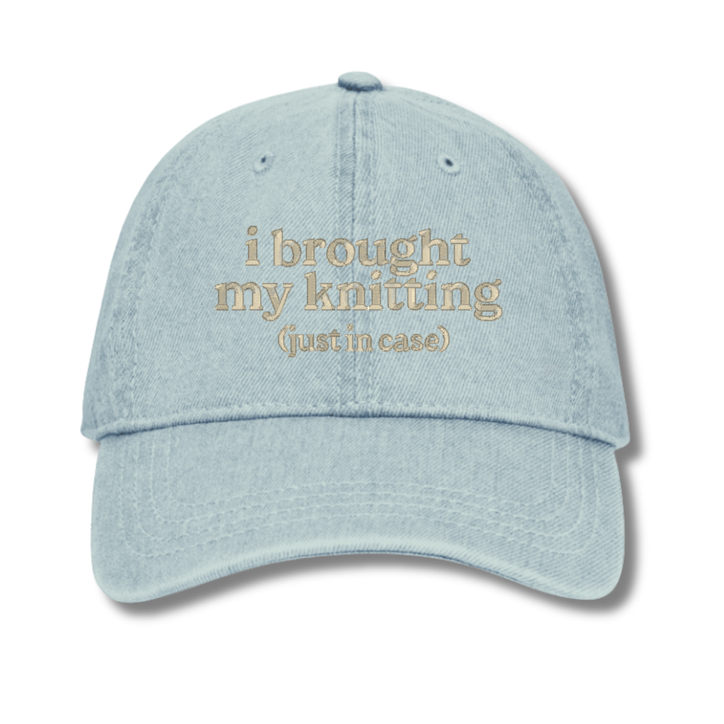 Light blue cap with text 'i brought my knitting (just in case)' on a white background