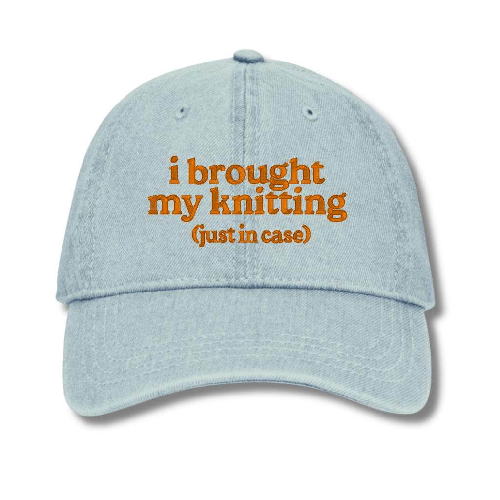 Light blue cap with orange text 'i brought my knitting (just in case)' on a white background