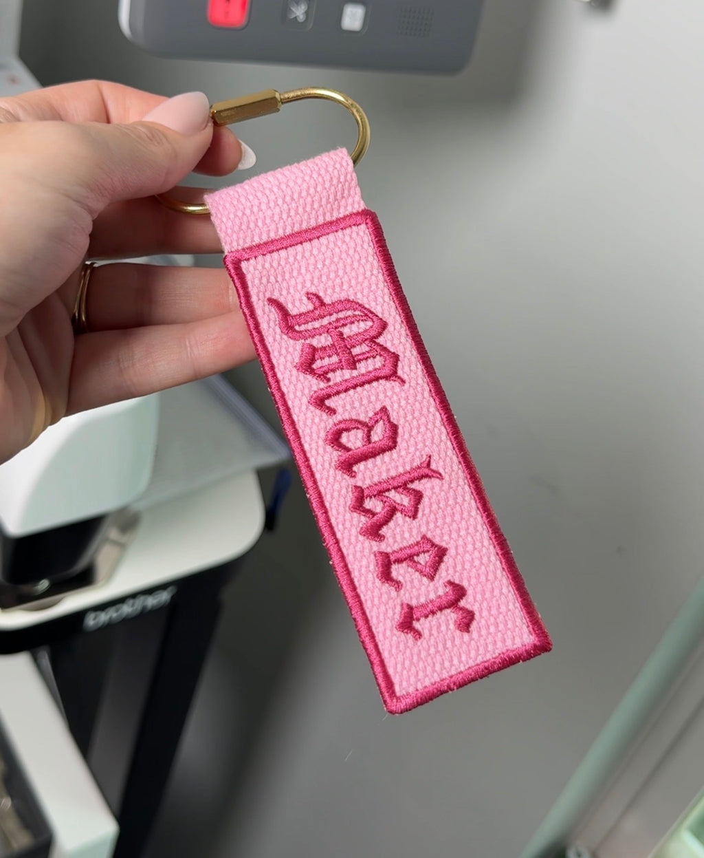 Pink keychain with text held by a hand against a blurred background