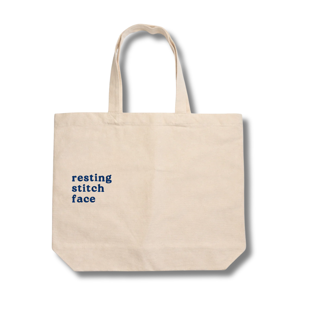 Beige tote bag with 'resting stitch face' text on a white background