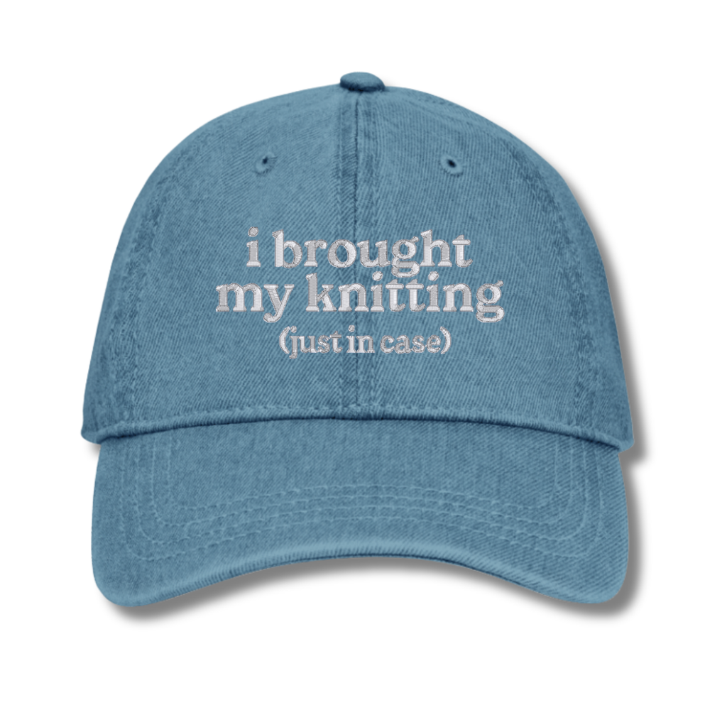 Blue cap with white text 'i brought my knitting (just in case)' on a white background