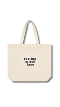 Beige tote bag with 'resting stitch face' text on a white background