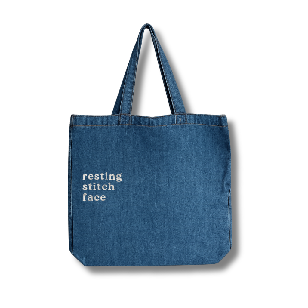Blue tote bag with 'resting stitch face' text on a white background