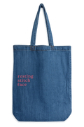 Blue denim tote bag with 'resting stitch face' text on a white background