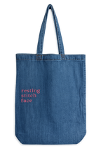 Blue denim tote bag with 'resting stitch face' text on a white background