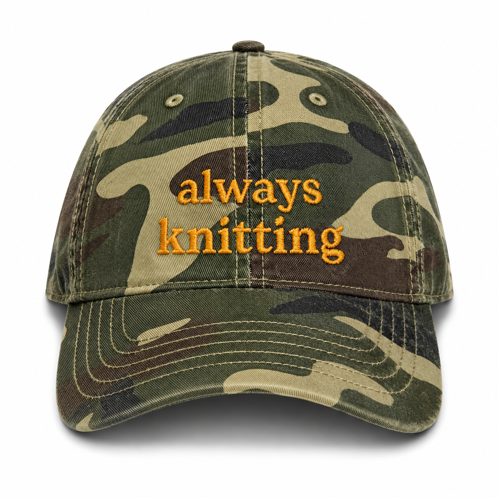 Camouflage cap with 'always knitting' text on a white background