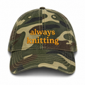 Camouflage cap with 'always knitting' text on a white background