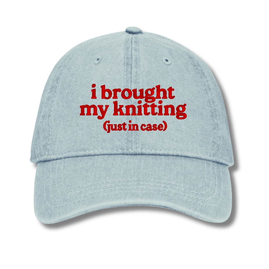 Light blue cap with red text 'i brought my knitting (just in case)' on a white background