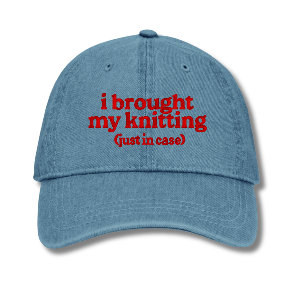 Blue cap with red text 'i brought my knitting (just in case)' on a white background