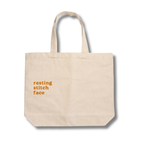Beige tote bag with 'resting stitch face' text on a white background