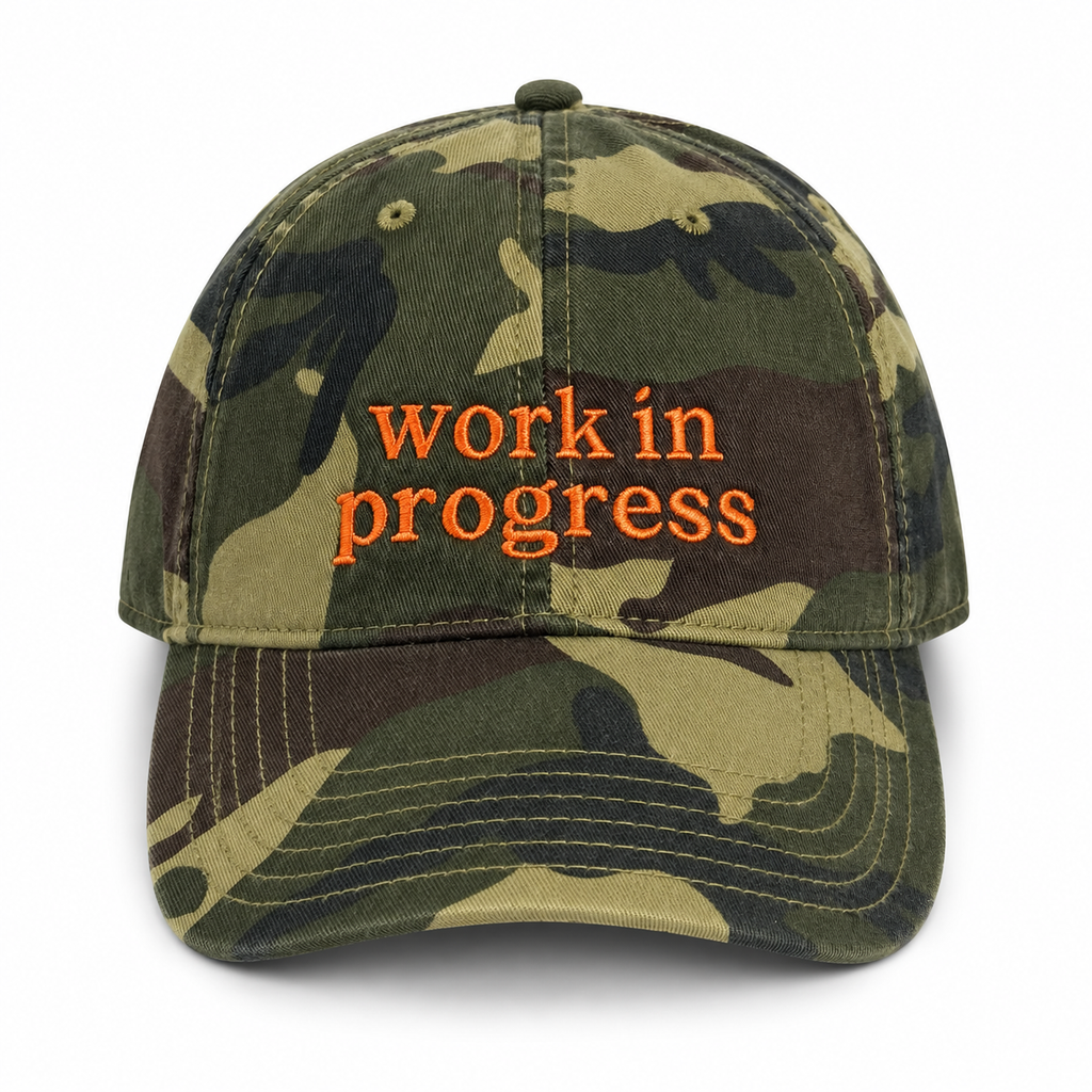 Camouflage cap with 'work in progress' text on a white background