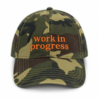 Camouflage cap with 'work in progress' text on a white background