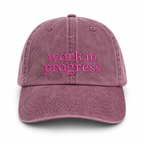 Pink cap with 'work in progress' text on a white background