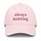 Pink cap with 'always knitting' text on a white background