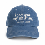 Blue cap with white text 'i brought my knitting (just in case)' on a white background