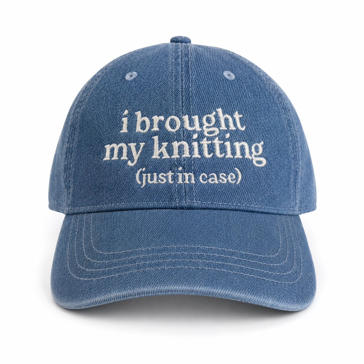 Blue cap with white text 'i brought my knitting (just in case)' on a white background