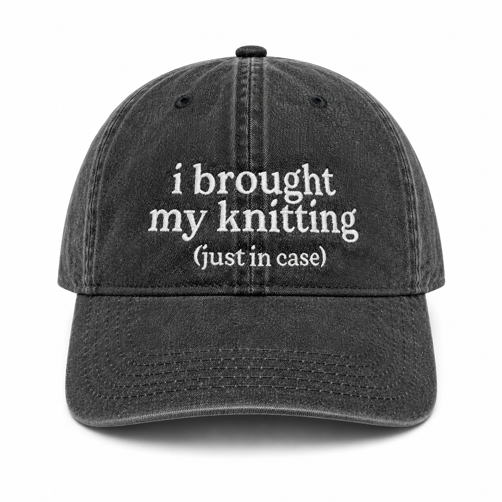 Black cap with white text 'i brought my knitting (just in case)' on a white background