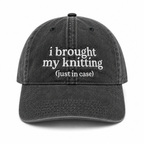 Black cap with white text 'i brought my knitting (just in case)' on a white background