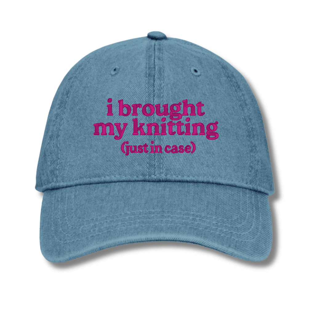 Blue cap with pink text 'i brought my knitting (just in case)' on a white background