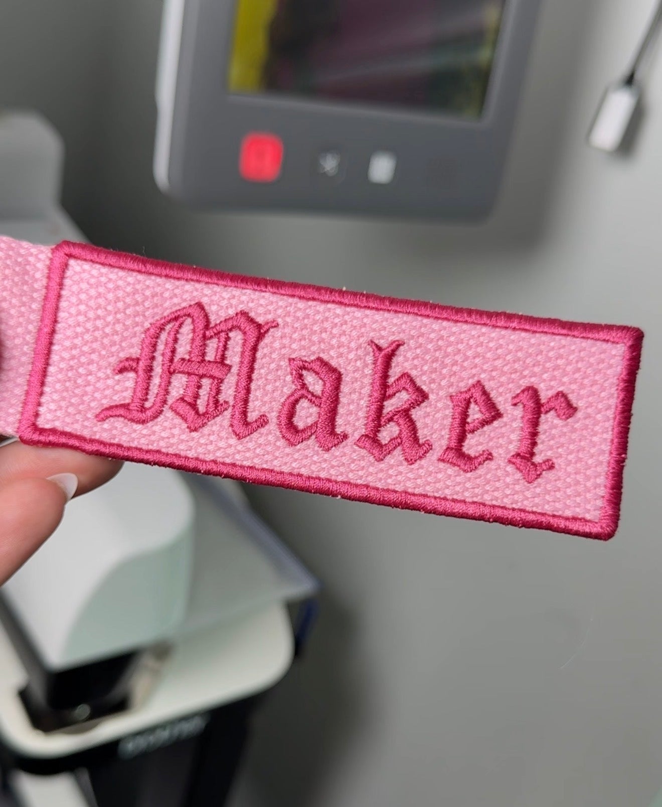 Pink patch with 'Maker' text held in front of a sewing machine.