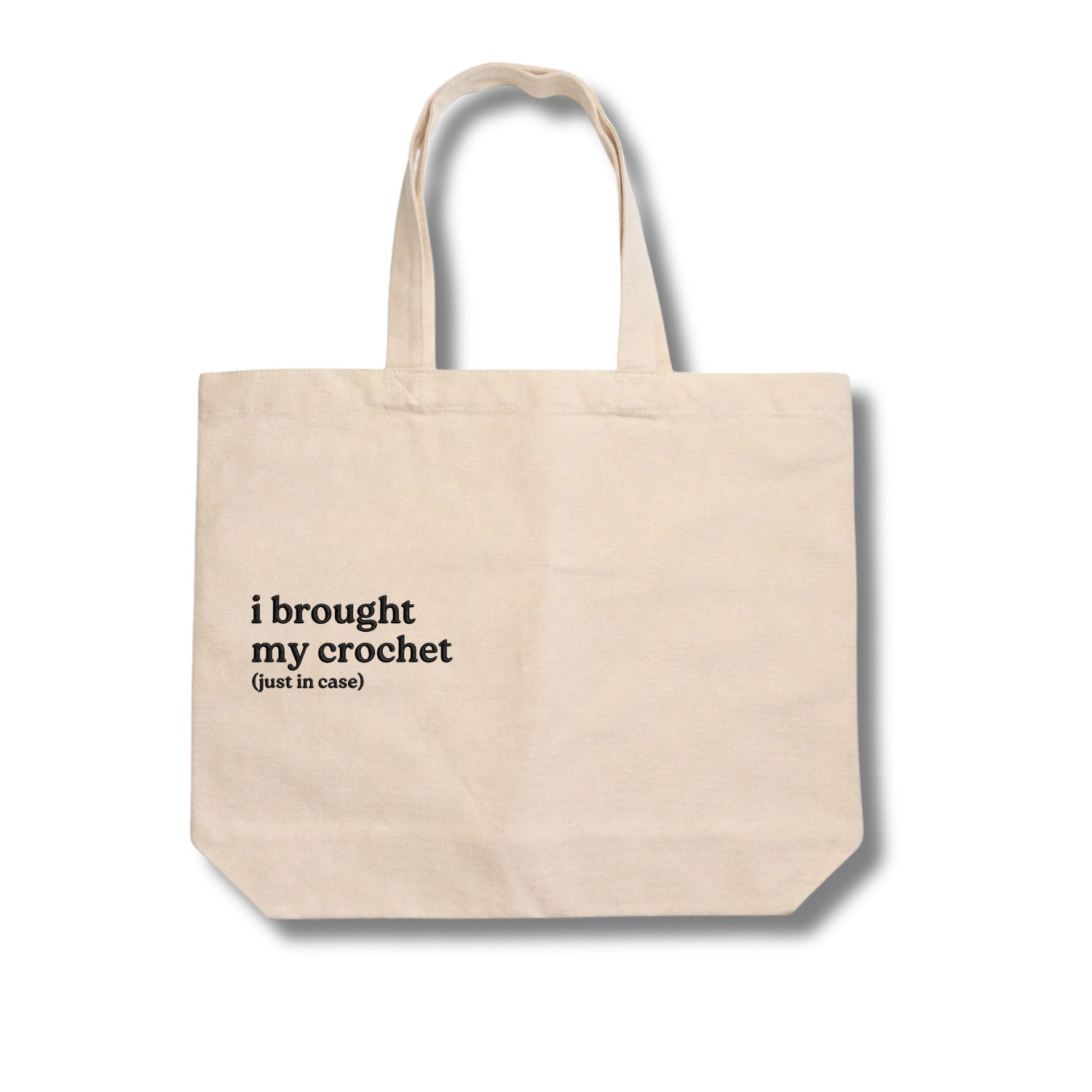 Beige tote bag with text 'i brought my crochet (just in case)' on a white background