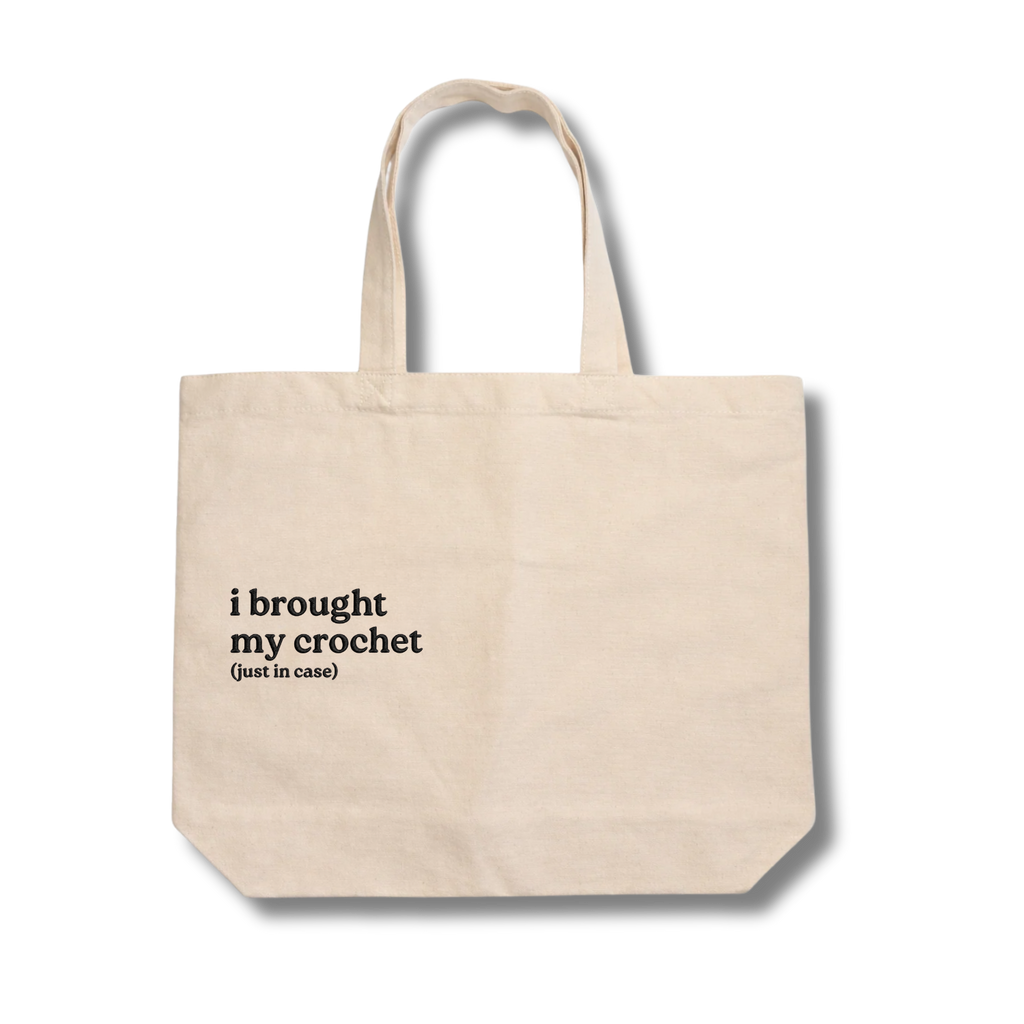 Beige tote bag with text 'i brought my crochet (just in case)' on a white background