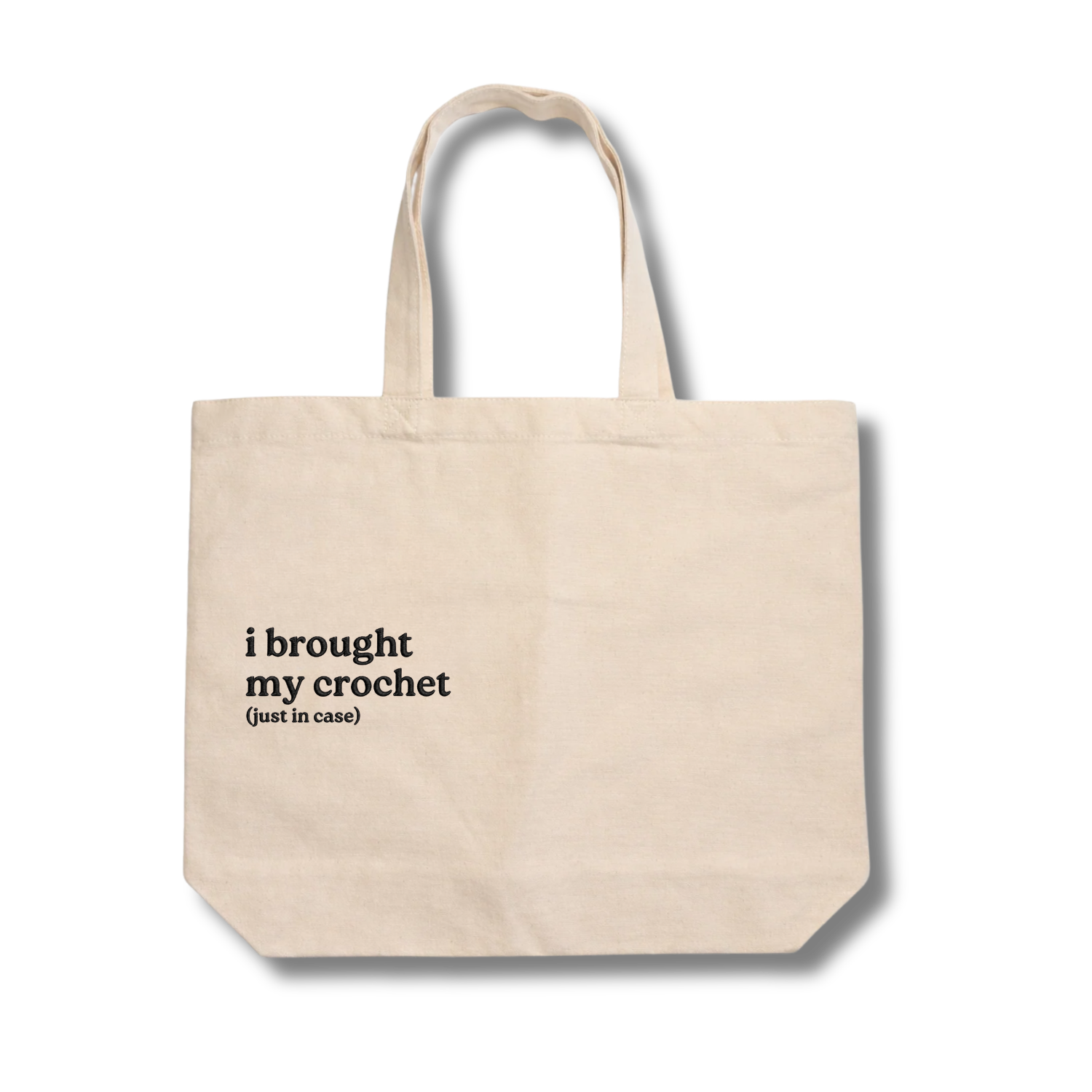 Beige tote bag with text 'i brought my crochet (just in case)' on a white background