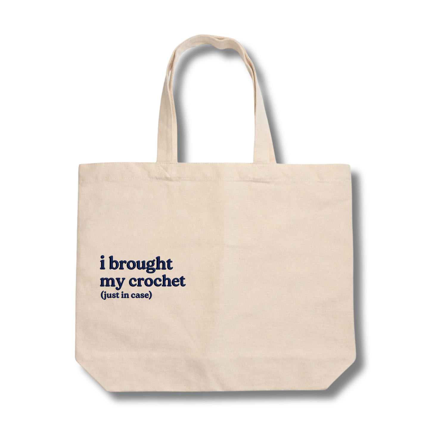 Beige tote bag with text 'i brought my crochet (just in case)' on a white background