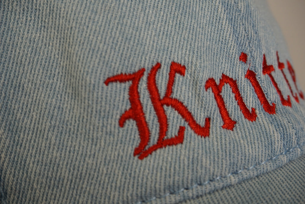 Light blue denim cap with red embroidered text on a blurred background