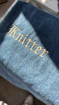 Blue fabric with 'Knitter' embroidered in taupe thread