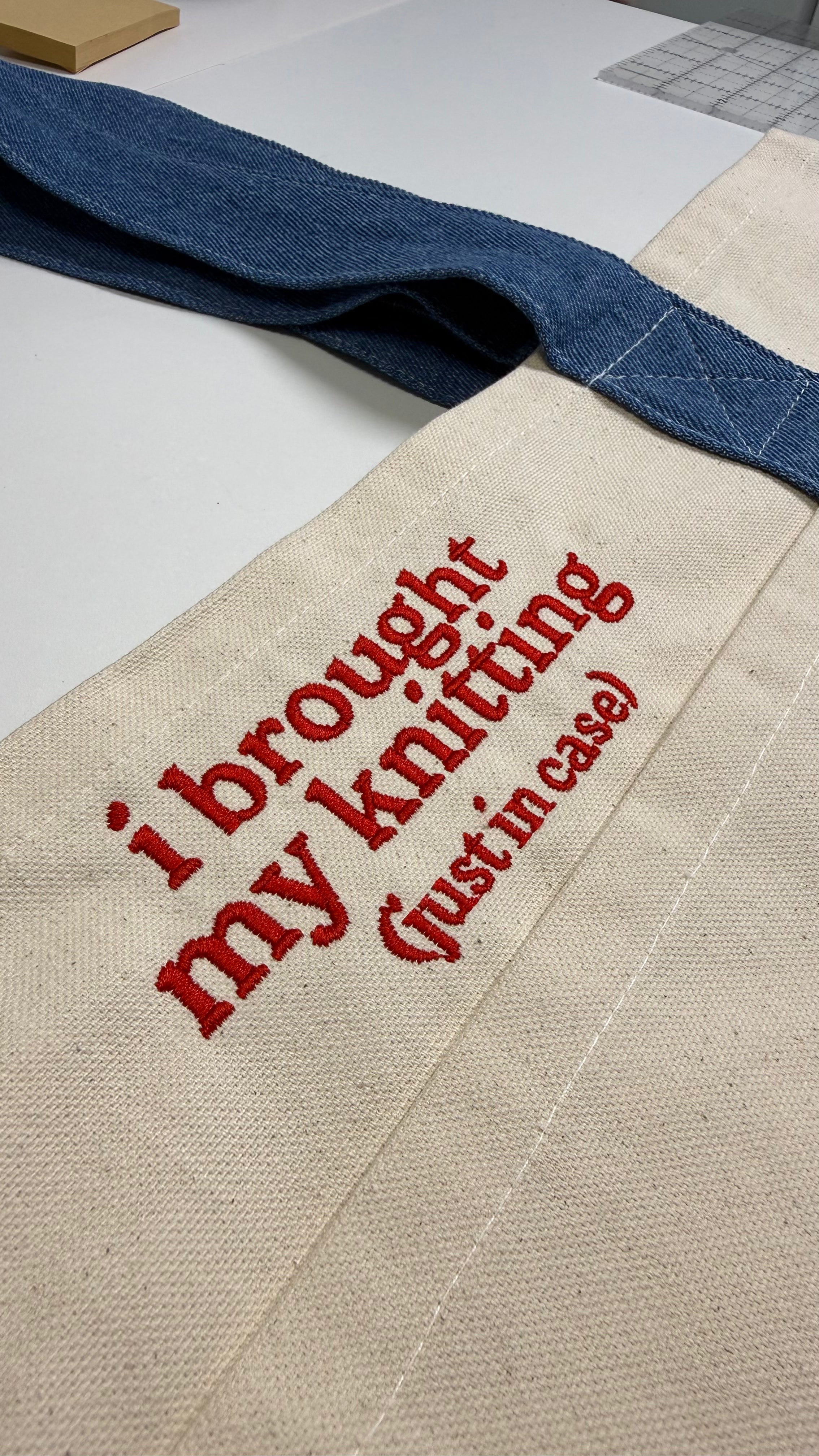 Textile bag with 'I brought my knitting (just in case)' text on a laptop keyboard background