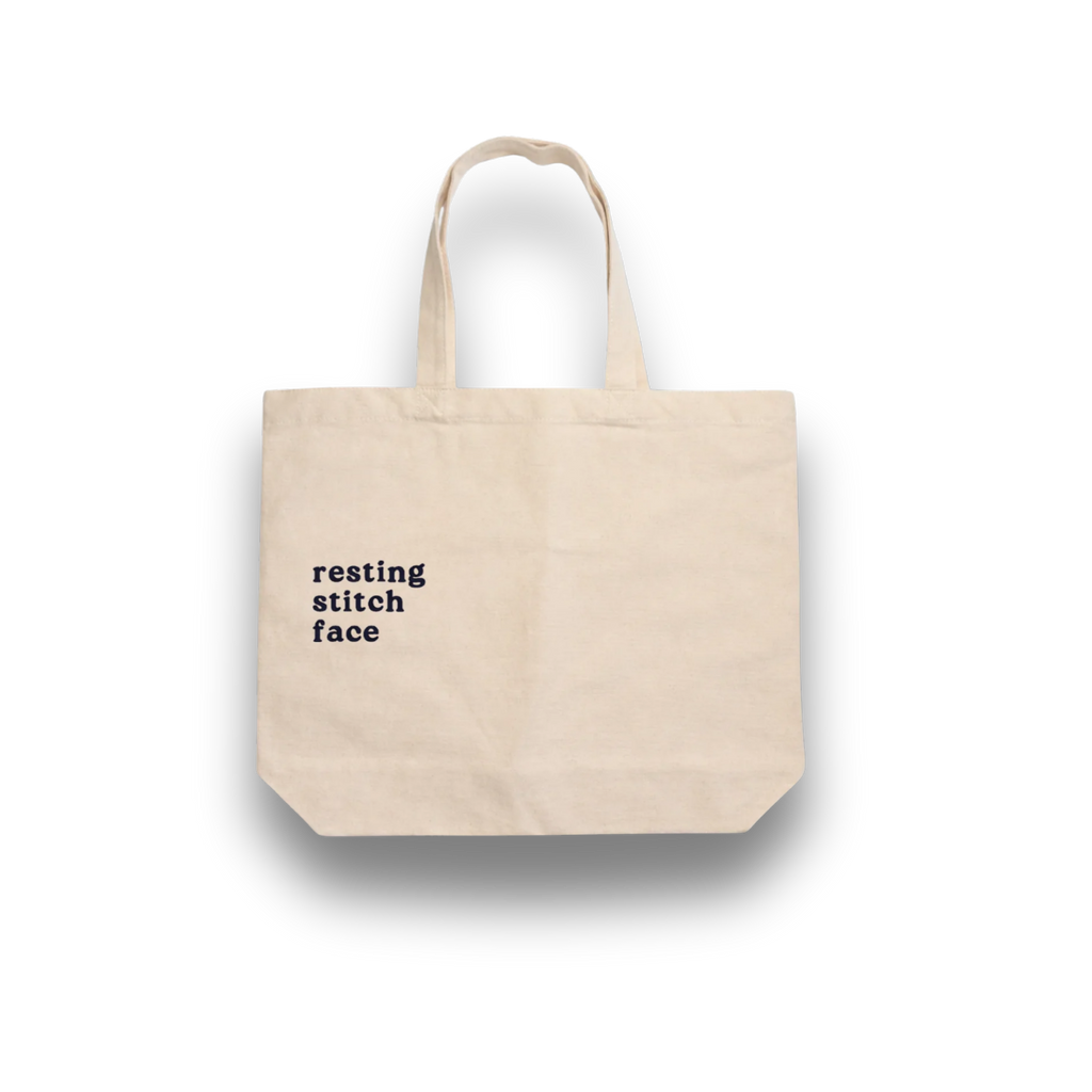 Beige tote bag with 'resting stitch face' text on a white background