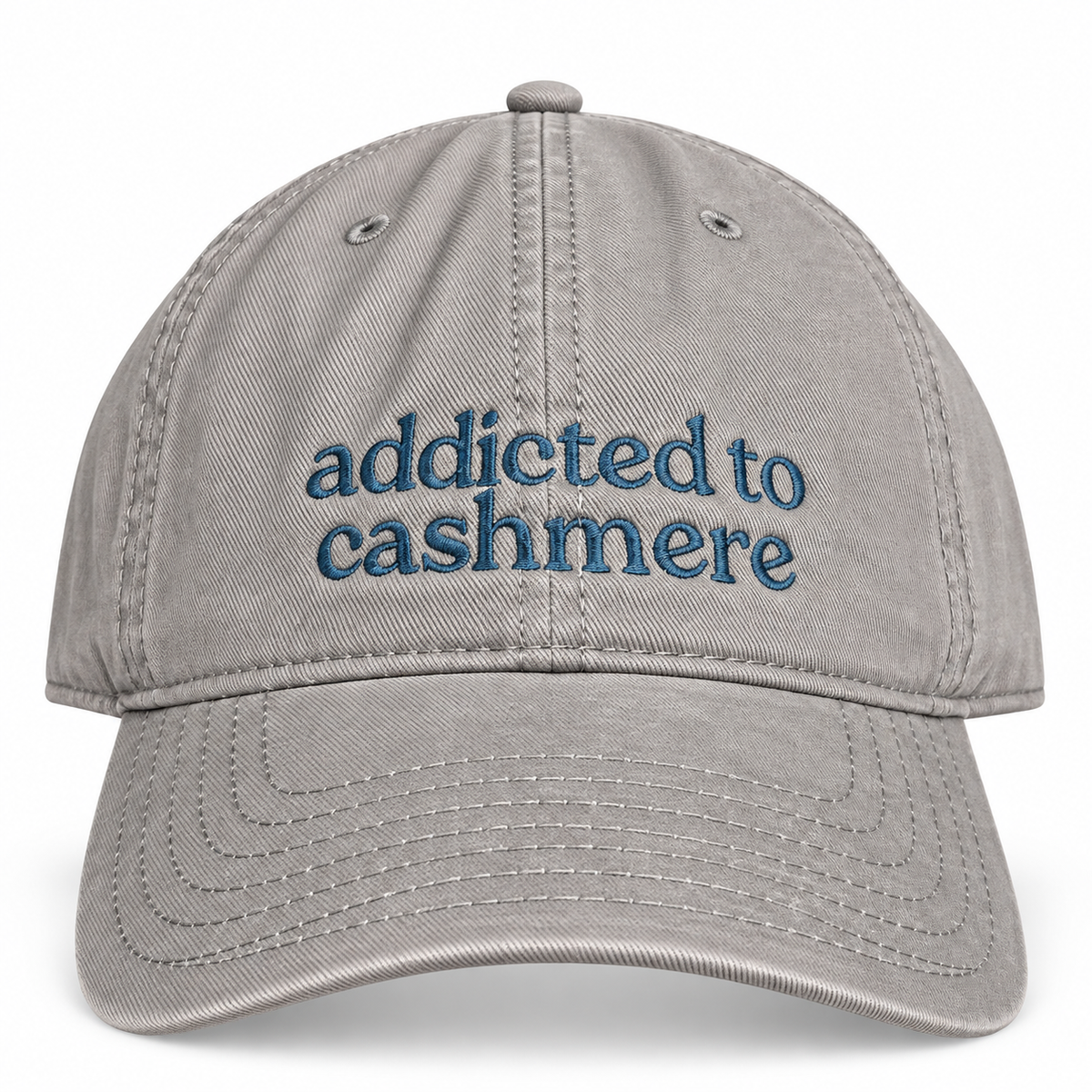 A light gray cotton baseball cap with blue embroidered text reading 'addicted to cashmere' on the front, shown against a plain white background.