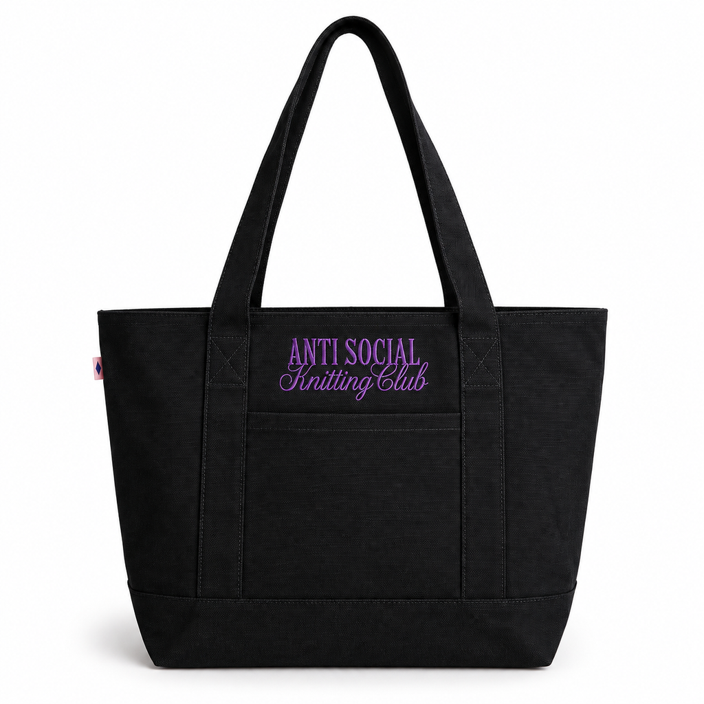 A black canvas tote bag with dual shoulder straps, featuring purple embroidered text on the front pocket that reads 'ANTI SOCIAL Knitting Club' on a clean white background.