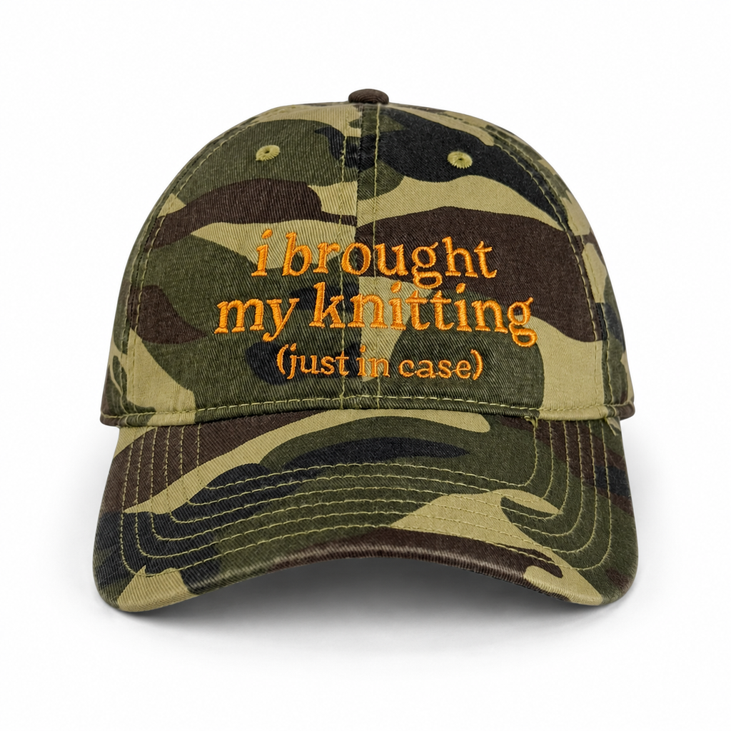 Camouflage cap with orange text 'i brought my knitting (just in case)' on a white background