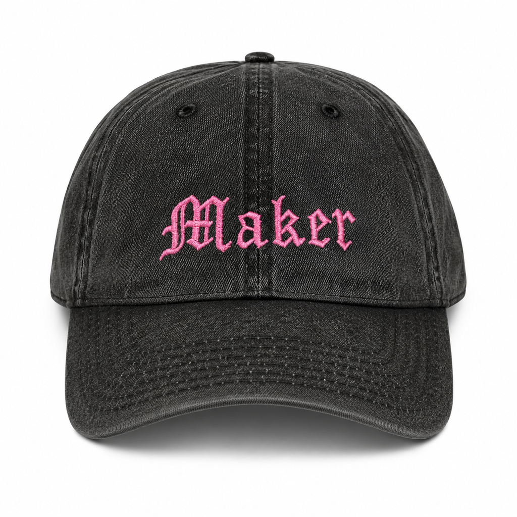 Black cap with 'Maker' embroidered in pink on a white background
