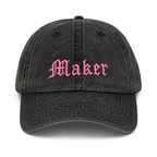 Black cap with 'Maker' embroidered in pink on a white background