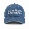 Blue denim cap with white text 'catch floats, not feelings' on a white background