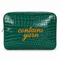A green crocodile-embossed zippered pouch with the words 'contains yarn' written in gold cursive across the front, shown on a plain white background.
