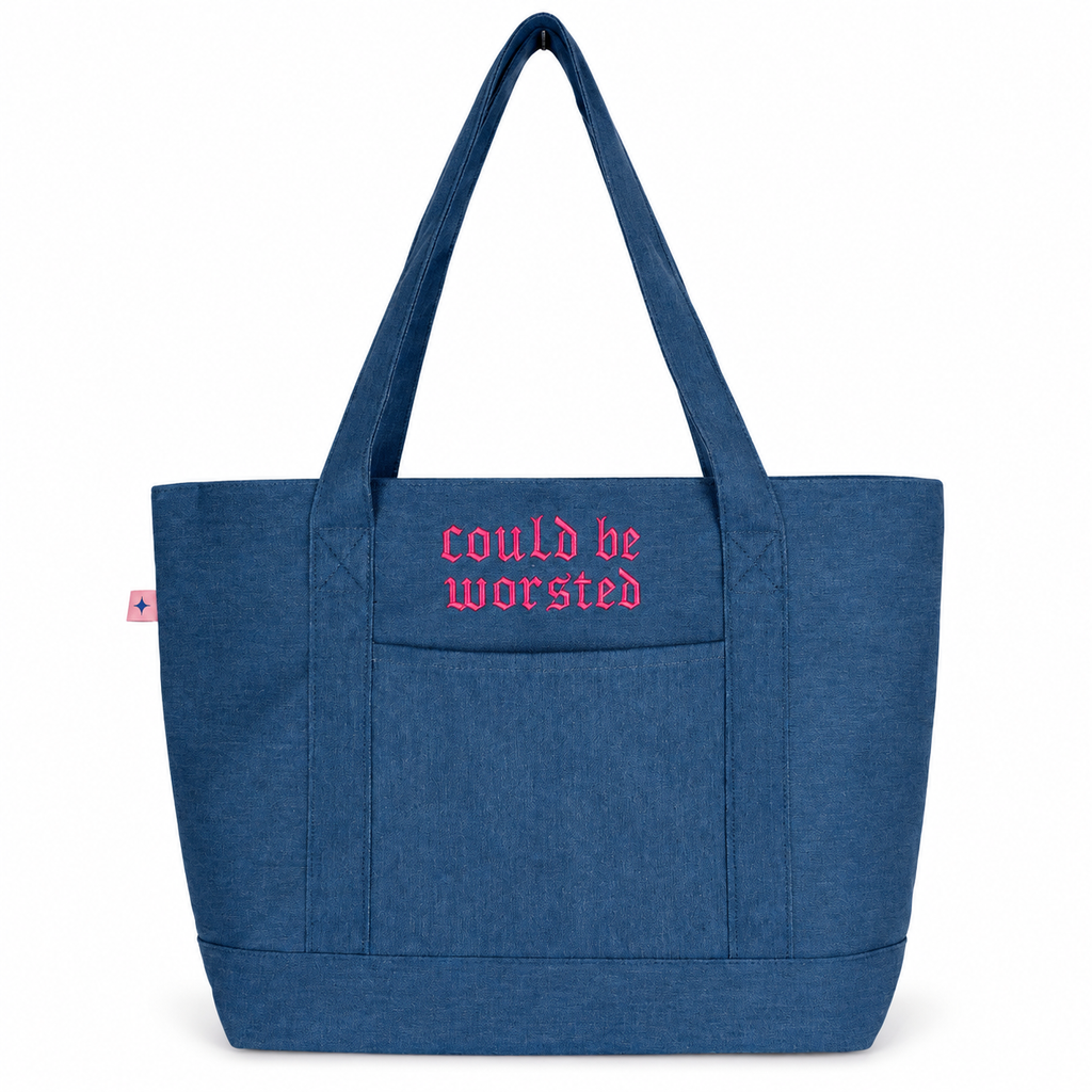 A blue canvas tote bag with long shoulder straps and pink gothic-style embroidered text reading 'could be worsted' on the front pocket, shown on a plain white background.