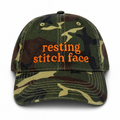 Camouflage cap with 'resting stitch face' text on a white background