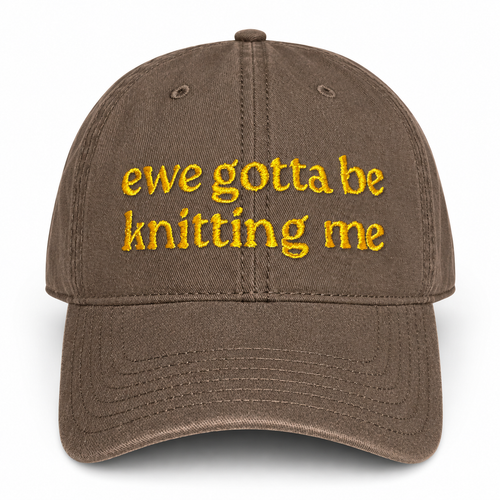 A brown baseball cap with yellow embroidered text reading 'ewe gotta be knitting me' on the front, shown against a plain white background.