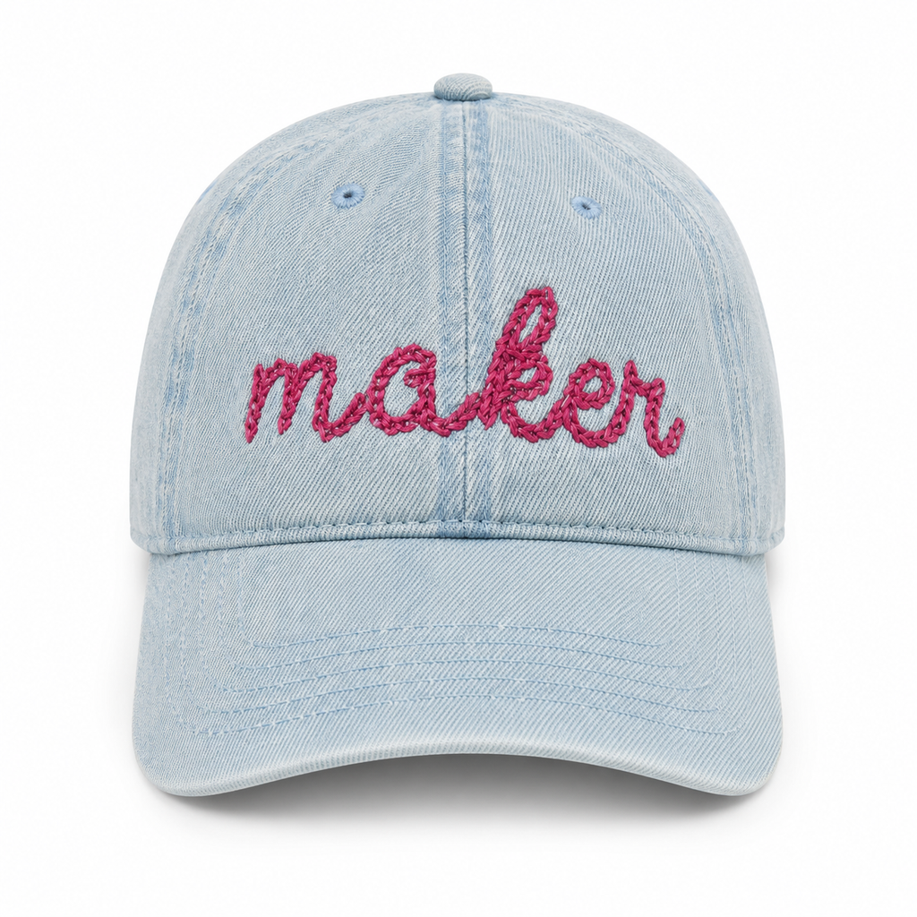 Light blue denim cap with 'maker' embroidered in pink on a white background