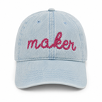Light blue denim cap with 'maker' embroidered in pink on a white background