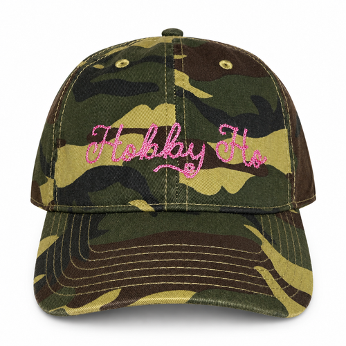 A classic dad-style baseball cap in a green, brown, and black camouflage pattern, featuring the phrase 'Hobby Ho' embroidered in pink script across the front panels.