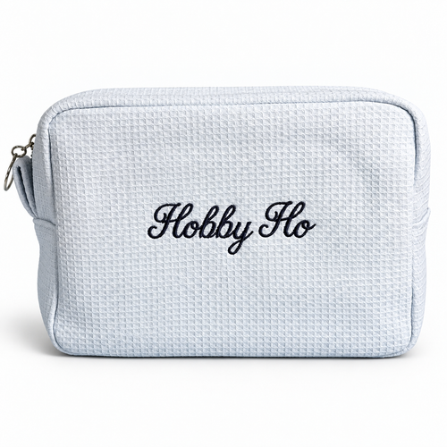 A light blue waffle-weave zippered pouch with 'Hobby Ho' embroidered in black script on the front, shown against a plain white background.