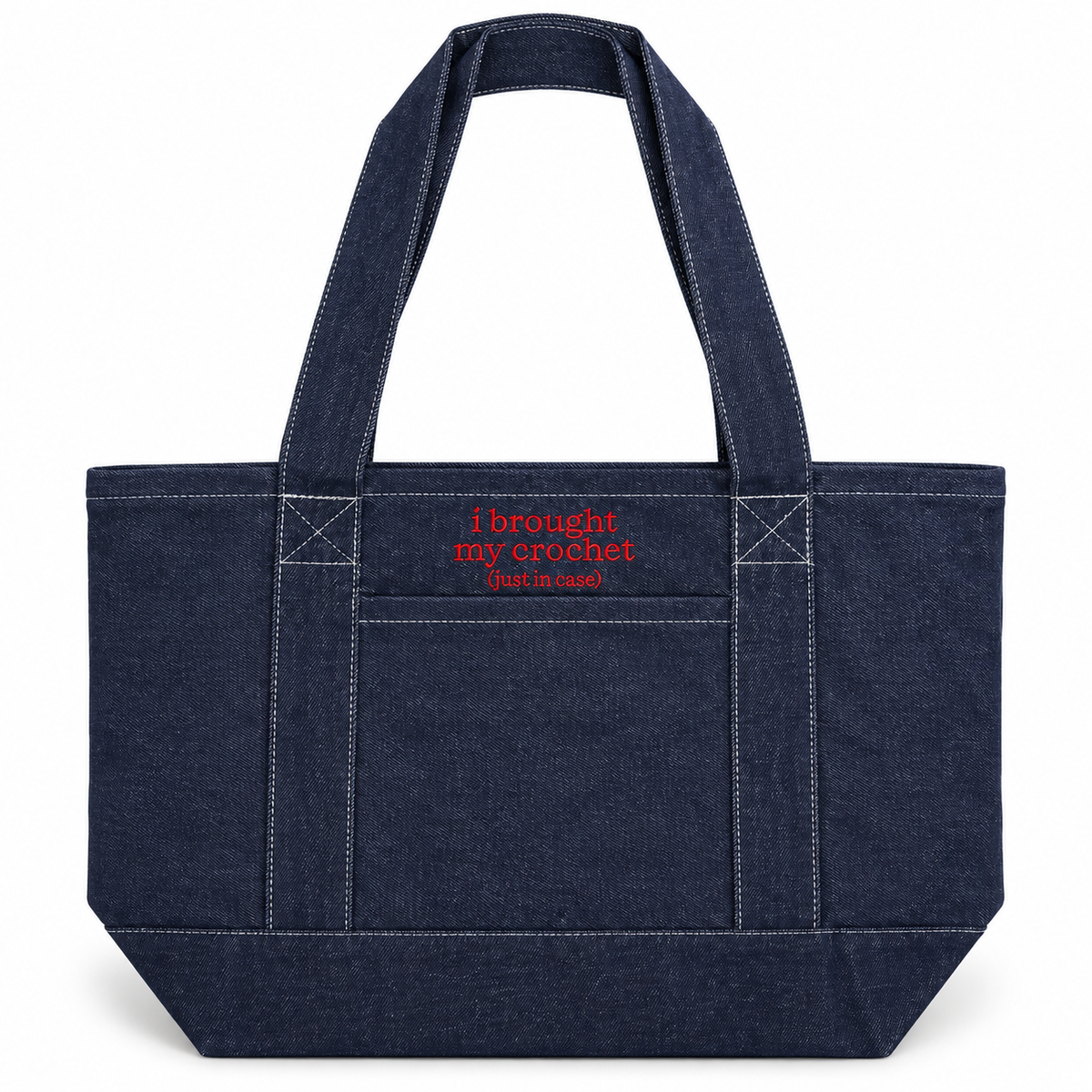 A dark indigo denim tote bag with white contrast stitching, featuring a front pocket with red embroidered text that reads 'I brought my crochet (but in blue)'.