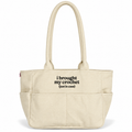 A cream-colored canvas tote bag with black printed text reading 'i brought my crochet (just in case)' on the front pocket, set against a plain white background.