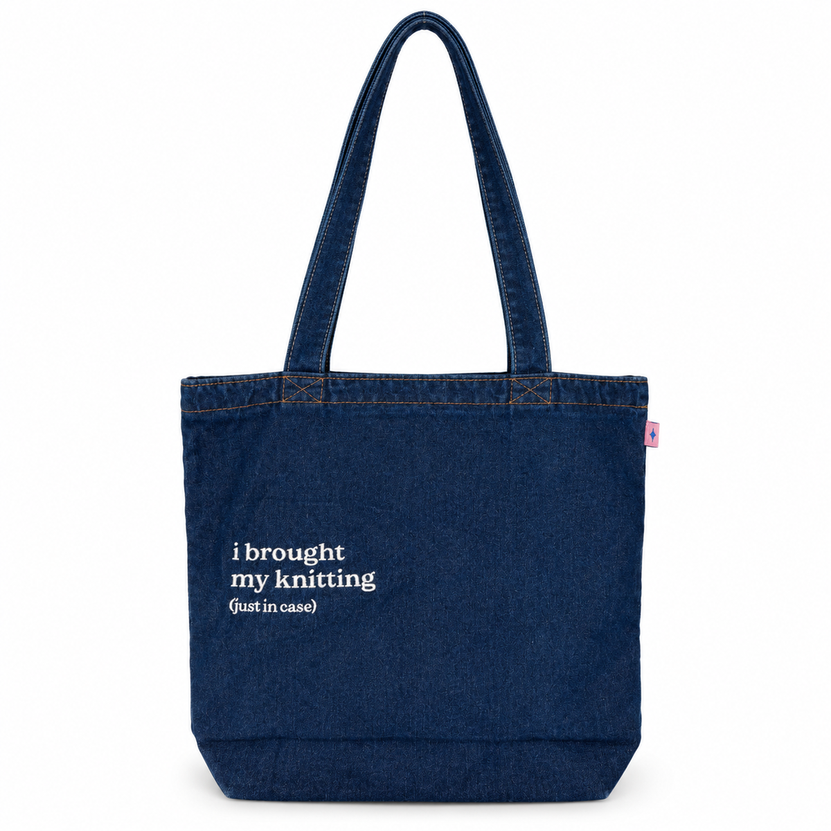 A dark blue denim tote bag with white printed text reading 'i brought my knitting (just in case)' on the front, set against a plain white background.